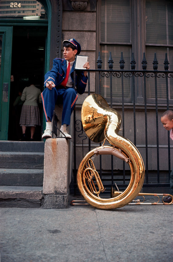 person sat on street of new york with a large trombone