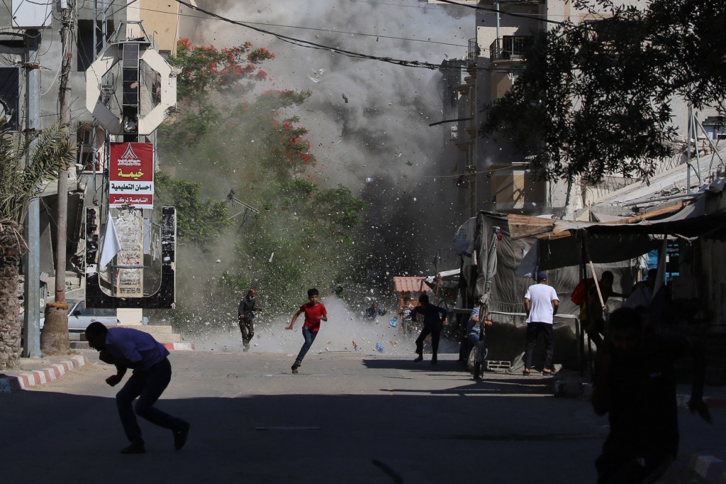 Palestinians rush for cover as debris flies around them after an Israeli strike on the
Bureij camp for Palestinian refugees in the central Gaza Strip on June 15, 2025. Image Credit: ©Eyad Baba / AFP via Getty Images
