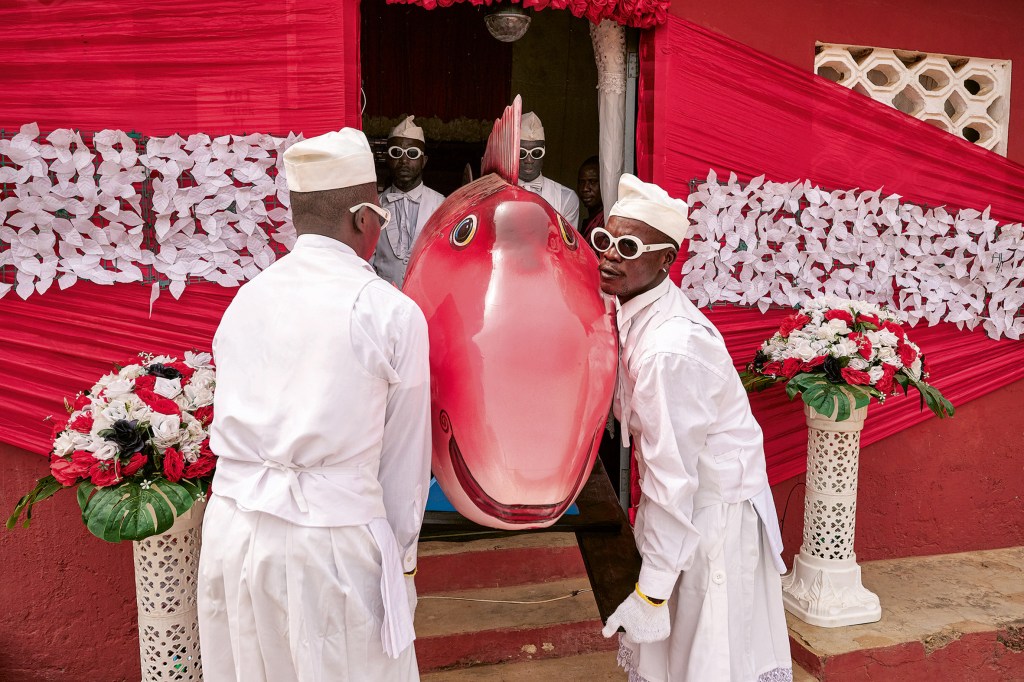 The eldest member of the family, a fishmonger, is honoured by her relatives with a fish coffin. Because the fish is too long for the prepared grave, the tail fin has to be sawn off. Greater Accra, 2024. (Coffin: Eric Kpakpo). Image Credit: Regula Tschumi