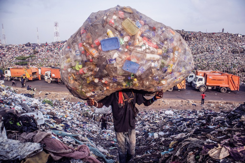 A waste miner climbs a hill of refuse at
Olusosun Landfill in Ikeja, Lagos, after
collecting waste freshly dumped from
a truck. 1 April 2025. Image Credit: Oyewole Lawal