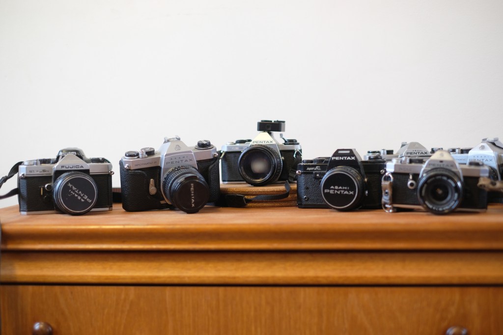 Photograph of several old film SLRs, one of which has a TTArtisan Light Meter