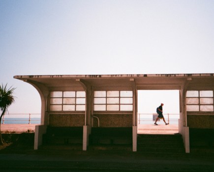 Street photograph of man walking past a bus shelter in Hastings, framed in a doorway, taken on Tudor 200 film and an Olympus XA2