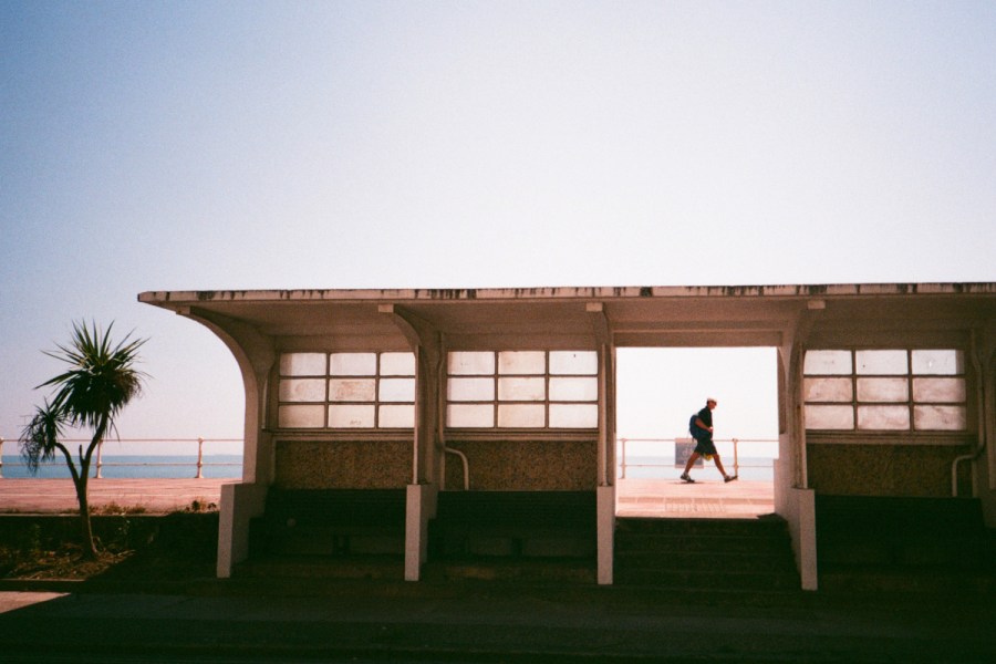Street photograph of man walking past a bus shelter in Hastings, framed in a doorway, taken on Tudor 200 film and an Olympus XA2
