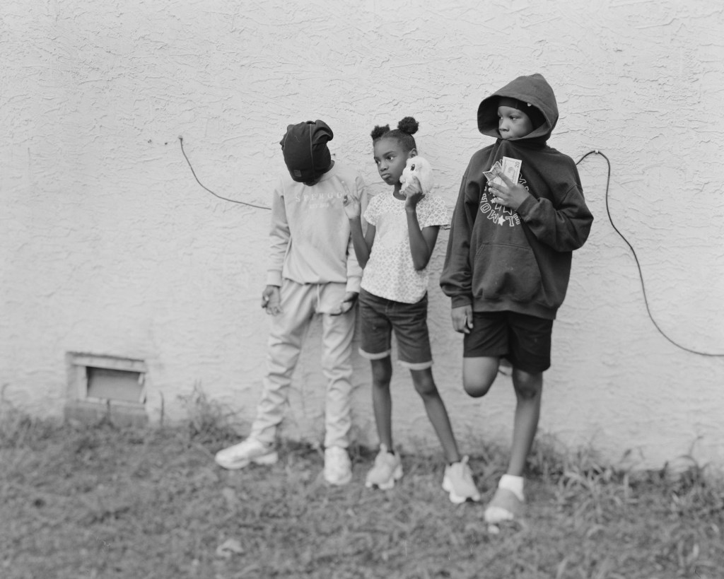This group asked Ci Song to take a picture of them, and he found this wall at the exterior of their house, with a cable appearing within the frame. He asked them to stand naturally, but they preferred this pose, with a toy and dollar bills.
