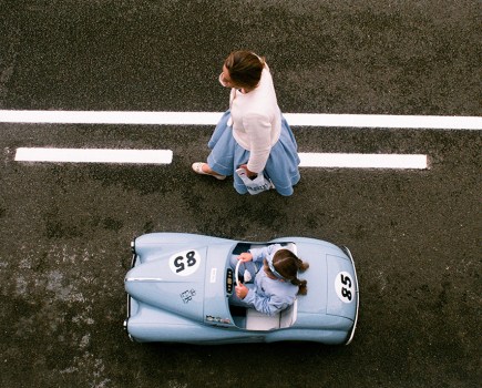 overhead photo of a small blue car and a person walking alongside it
