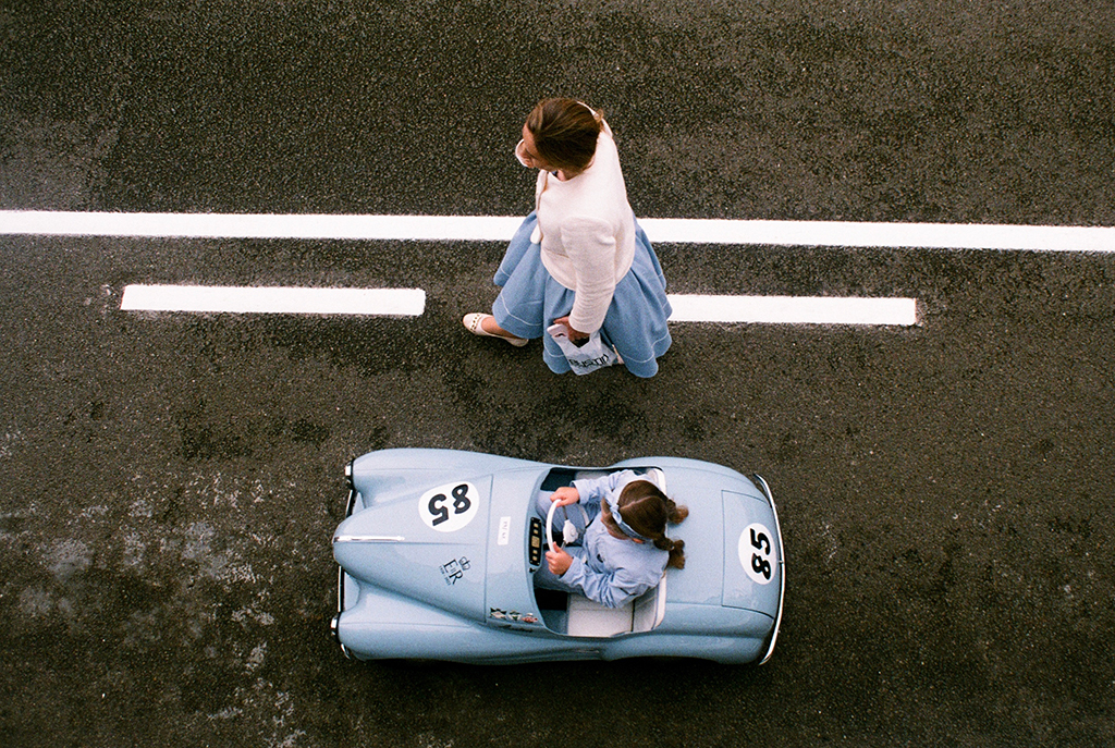 overhead photo of a small blue car and a person walking alongside it