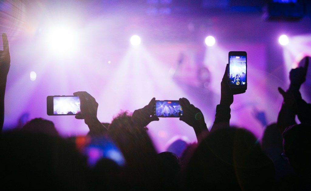 People recording videos and taking photos of a live rock and roll band using a smartphone