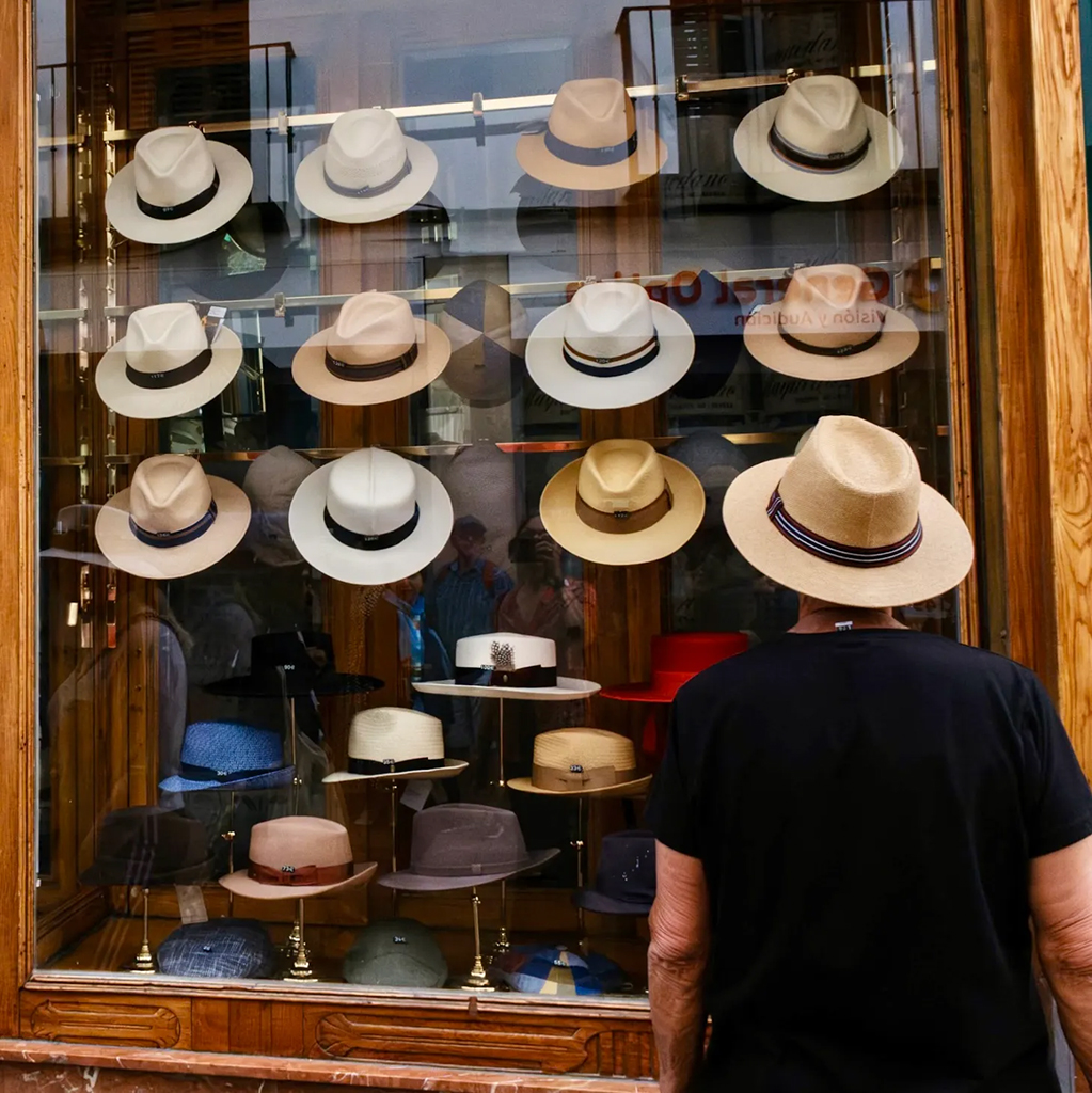 man in a hat looking at shop window full of more hats