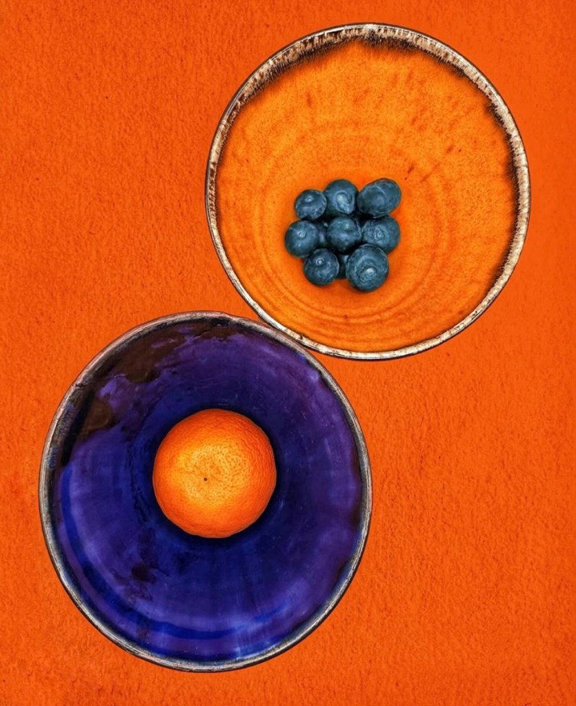 orange bowl with blueberries next to a blue bowl with a satsuma inside 