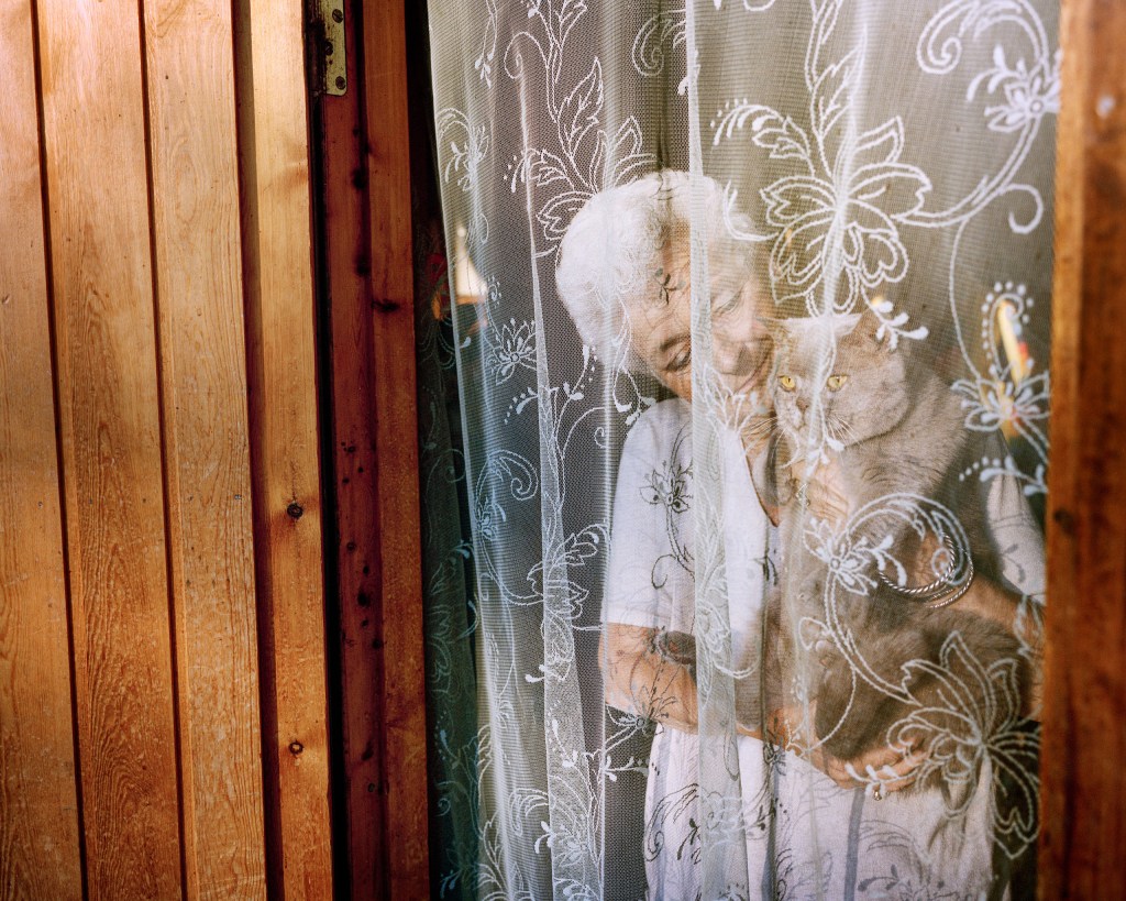 A woman holding a cat behind a net curtain
