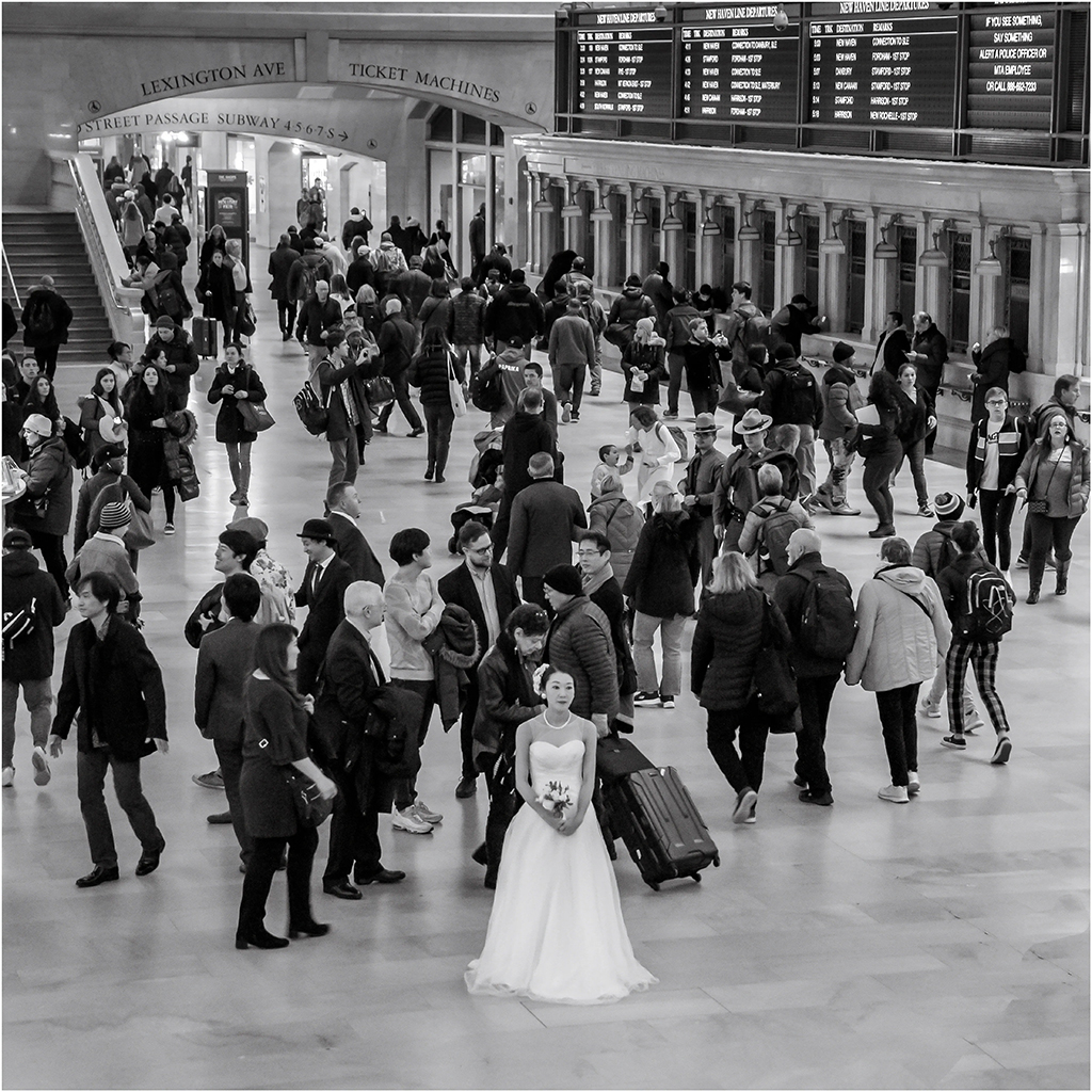 busy crowd in a train station with a bride in white dress amongst