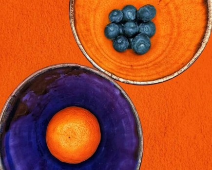 orange bowl with blueberries next to a blue bowl with a satsuma inside