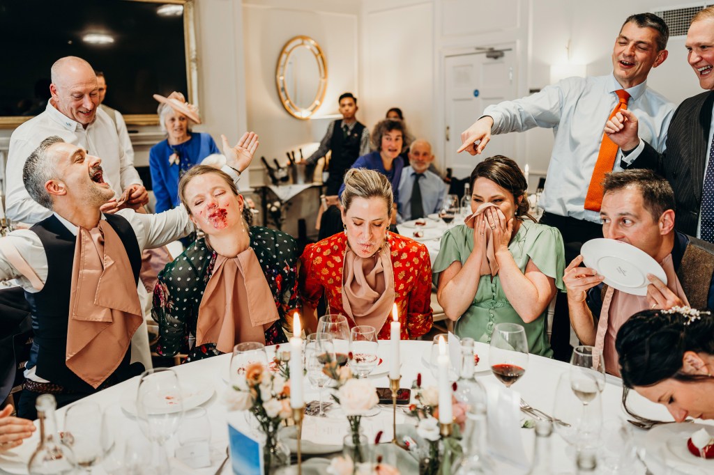 group photo of a table at an event laughing with food around their mouths