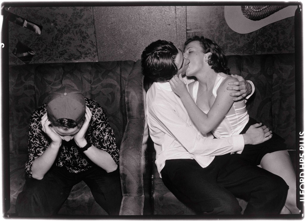two people kissing while a third person nearby covers their ears