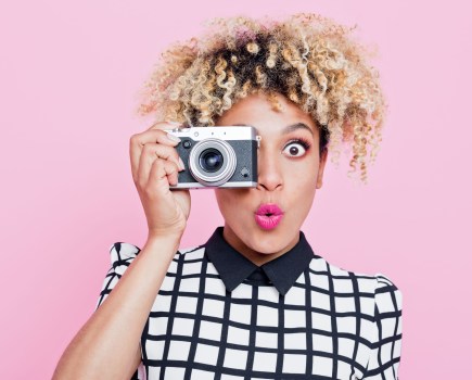 A woman holding a camera in front of a pink background