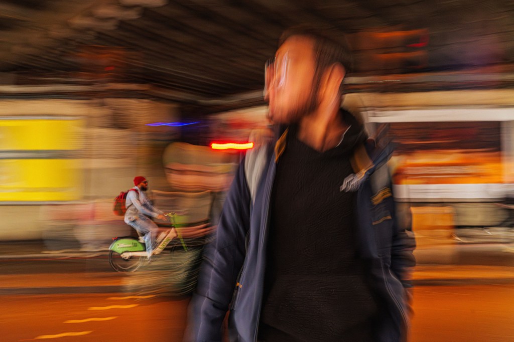 a slow shutter speed photo of a person standing and a cyclist in the bbackground