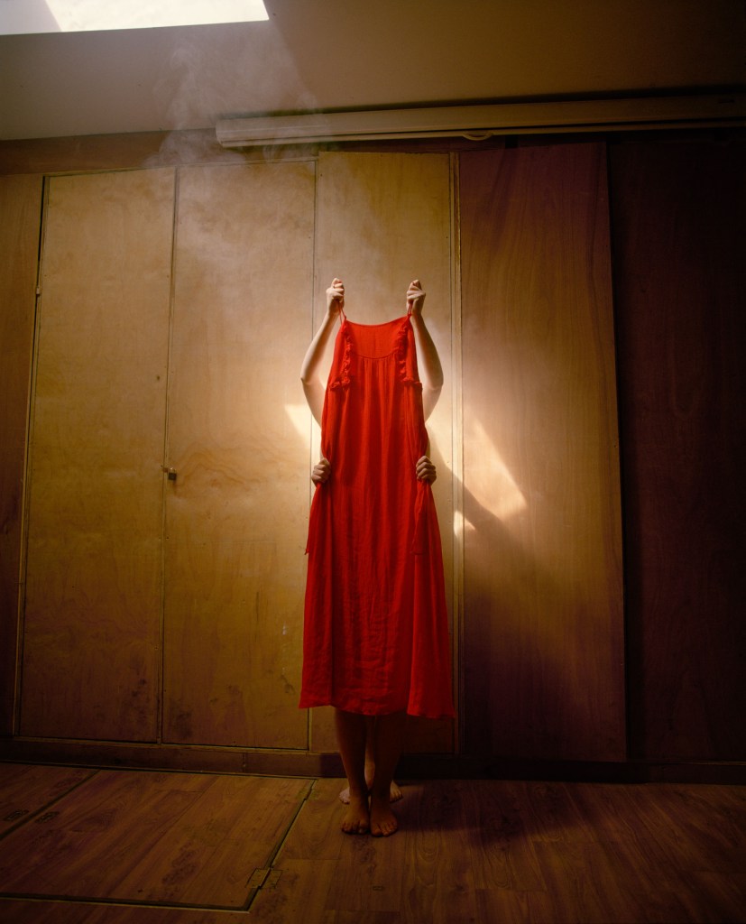 Colour photograph of a two unidentified people holding up a red dress.