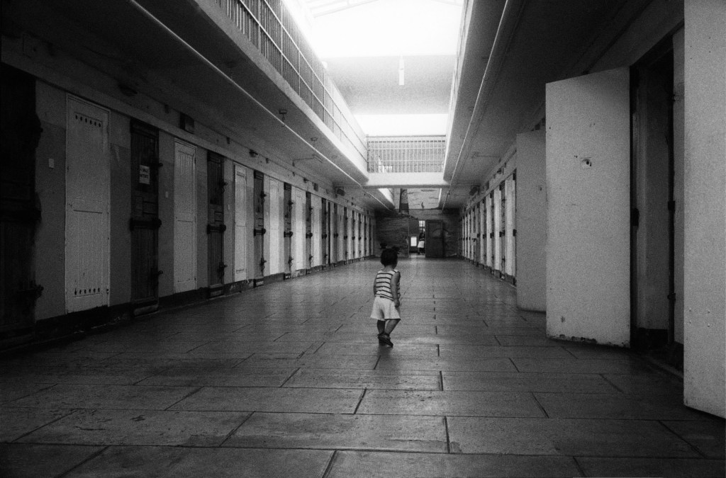 Black and white photograph of a toddler walking along a prison corridor.