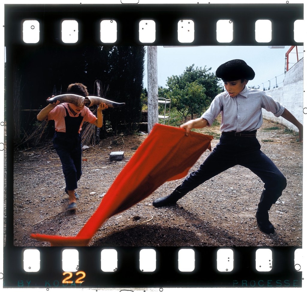 One boy holding a red cloth and another holding  bull horns