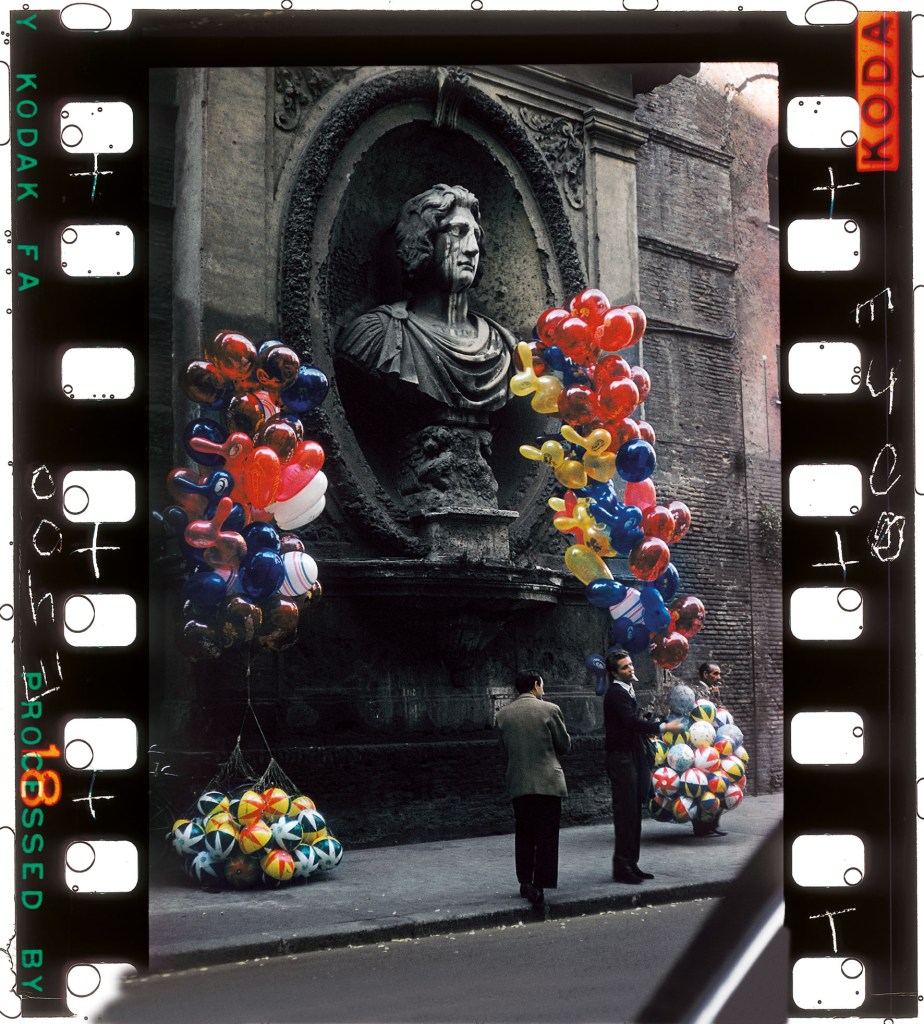 two men with a bunch of balloons in front of of the statue