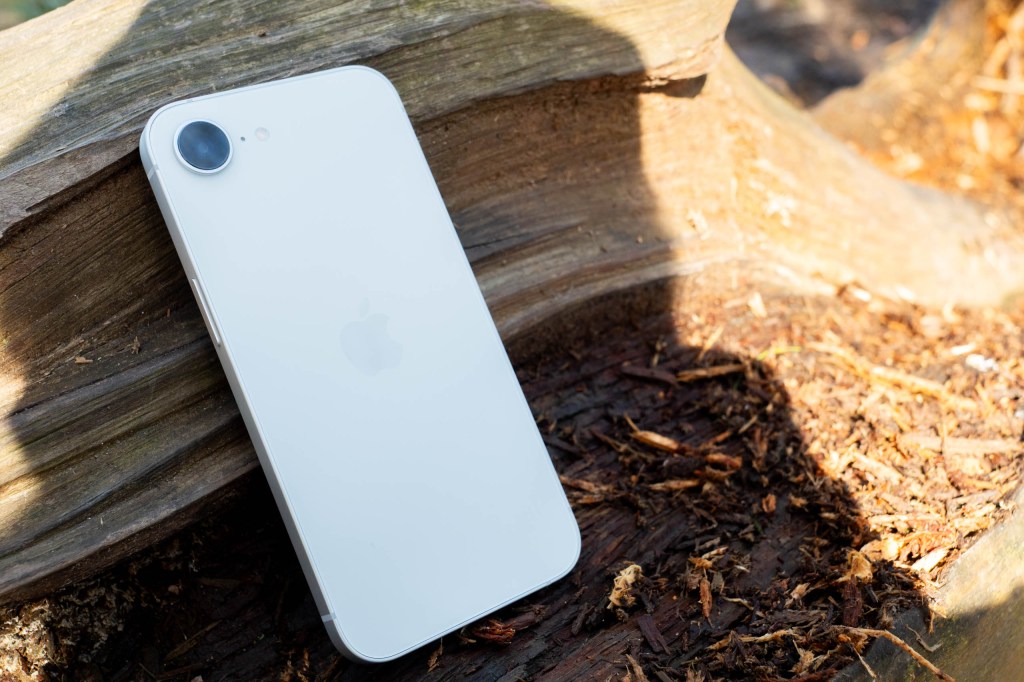 An iPhone 17e resting on a wooden log