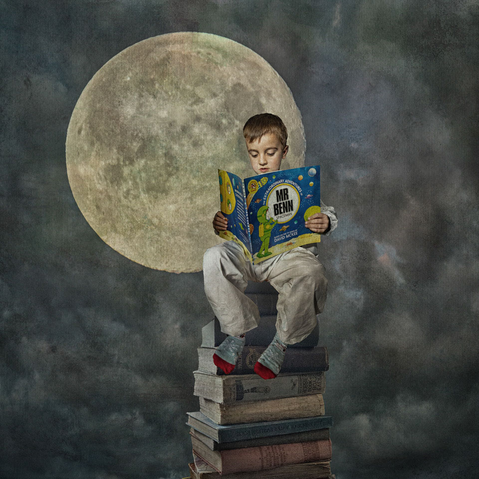 composite image of a boy dressed in a spacesuit sitting on a stack of books with the moon in the background