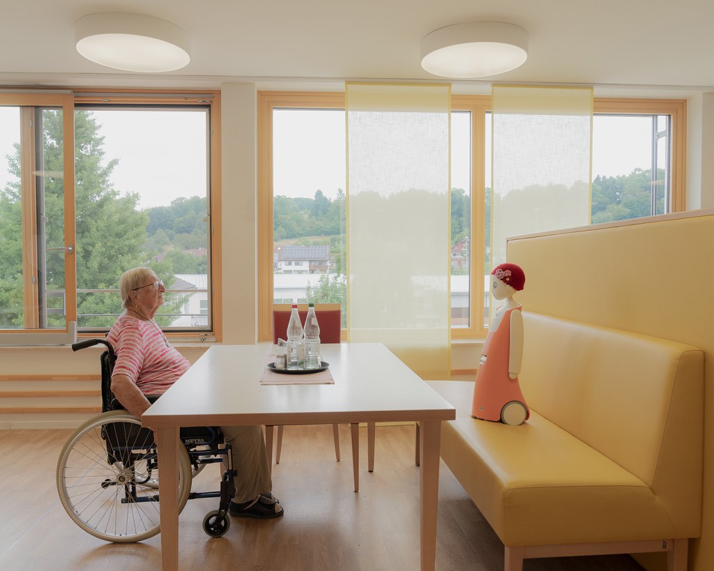 Waltraud talks with Emma, a social robot that recognizes faces and remembers past conversations. Though skeptical at first, Waltraud says she felt connected to Emma over time. Albershausen, Germany, 3 July 2025