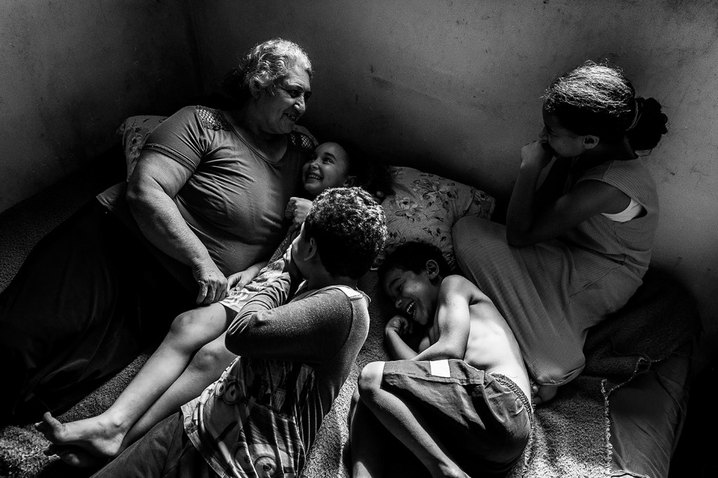Sandra Mara Siqueira rests with her grandchildren, Micael, Davi, Ana Flávia, and Vitória. Living in the Parque dos Lagos occupation since 2013, the family seeks land regularization to guarantee access to basic infrastructure. Colombo, Paraná, Brazil, 15 November 2025.