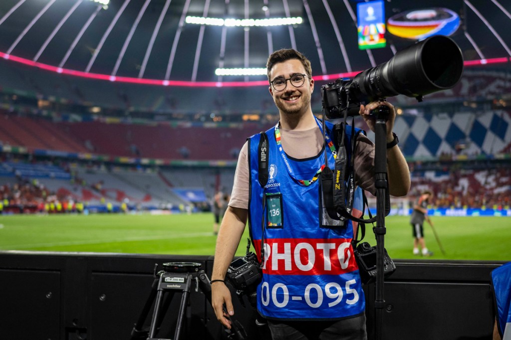 photographer stood pitchside with a large camera and lens on a monopod