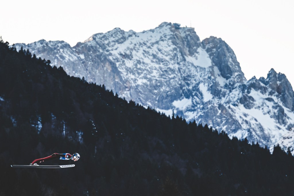 landscape photo of snowy mountain with skier mid air jump