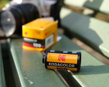 Photograph of Kodacolor 100 film canister and box with SLR camera visible in the background