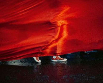 person in red sneaker walking behind a red fabric