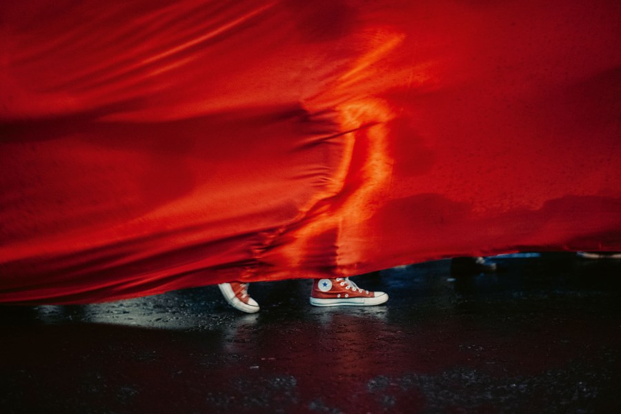 person in red sneaker walking behind a red fabric