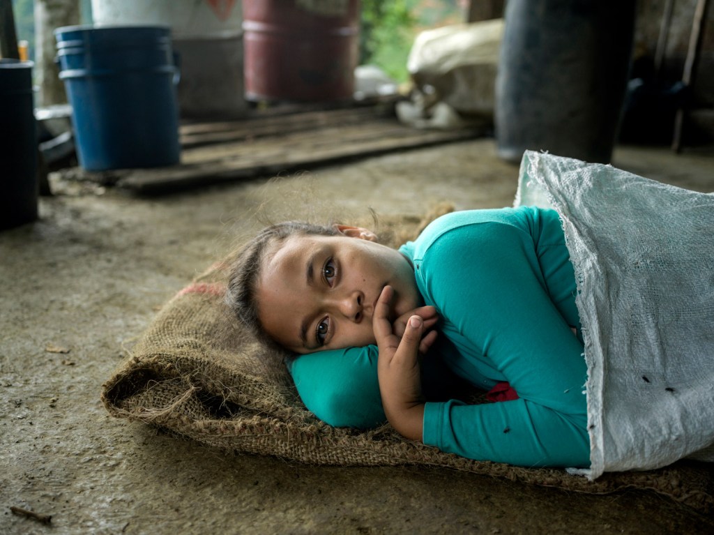 Diney Alexandra lies on the floor, taking a nap out of boredom at her father’s laboratory as the processing continues around her. It takes roughly 700 kilos of coca leaves along with substances such as cement (p. 32), ammonium, sulfuric acid, sodium permanganate, caustic soda, and large quantities of gasoline—to produce just a single kilo of coca paste. The aim of the entire process is to extract and isolate the leaf’s most desired and valuable component: the cocaine alkaloid. Antioquia and Cauca, Colombia, 2026. Image Credit: Mads Nissen