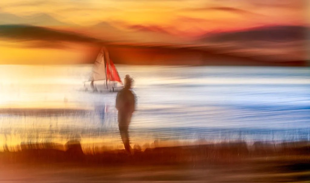 intentional camera movement landscape of sunset at the beach with boat and person in the centre