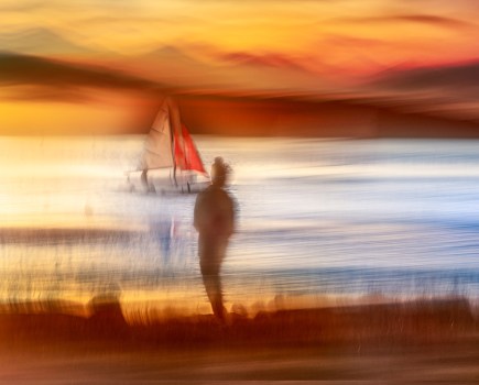 intentional camera movement landscape of sunset at the beach with boat and person in the centre