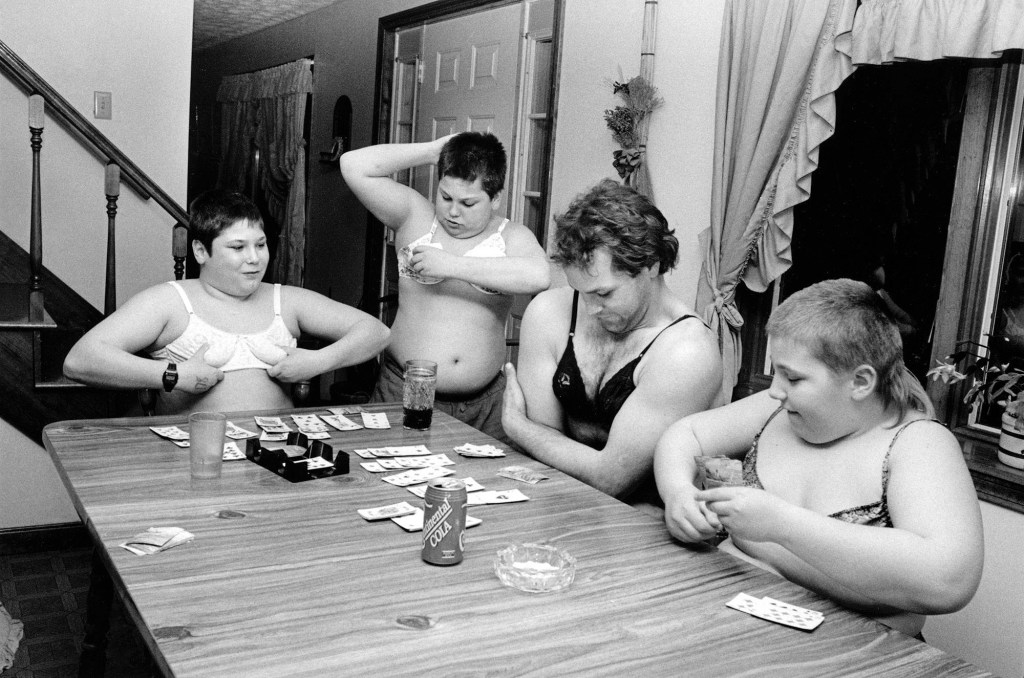 black and white phoyo f 4 boys trying on bras at a dinner table