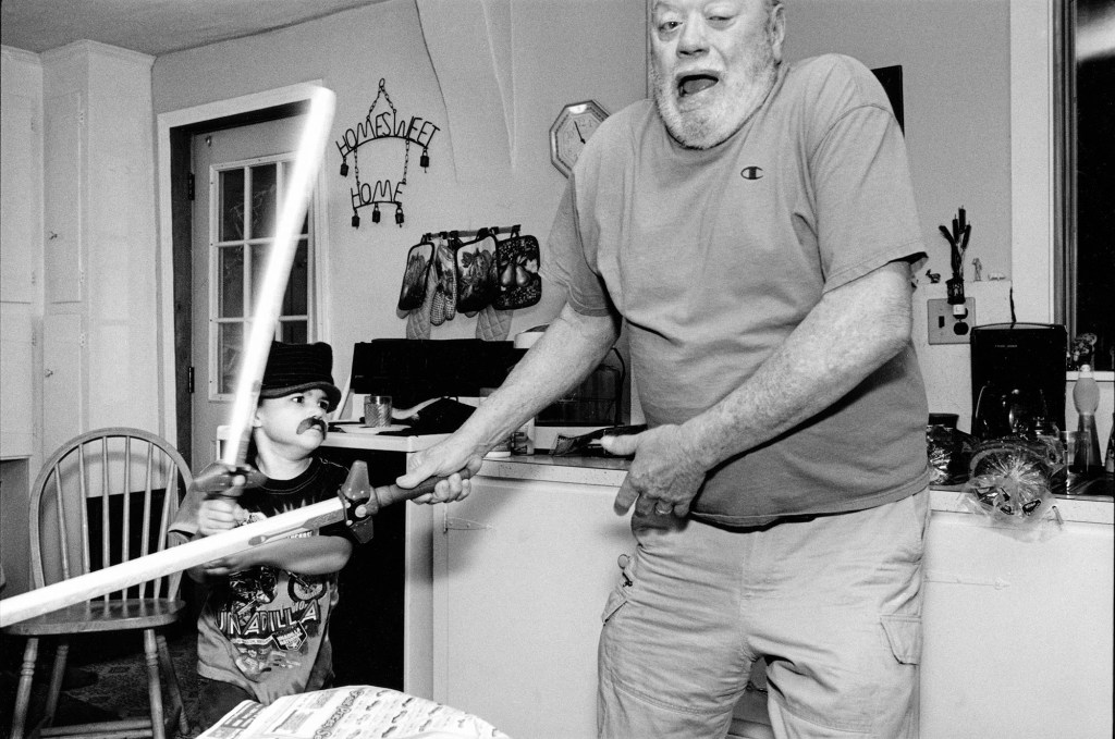 black and white photo og an older man holding a nerf sword