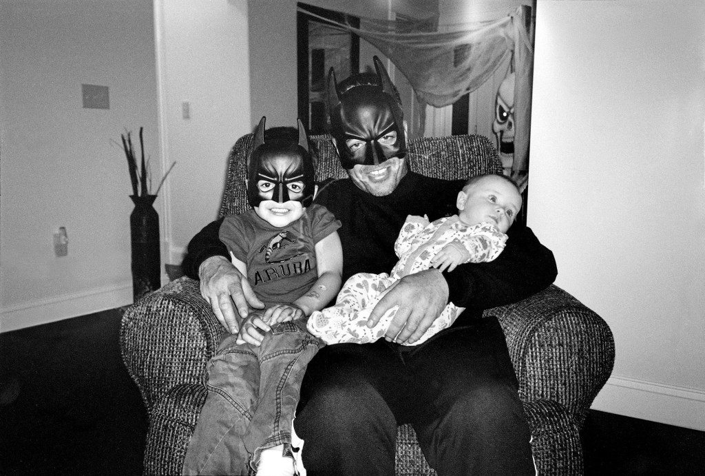 black and white photo of a man holding two children dressed in halloween costume masks
