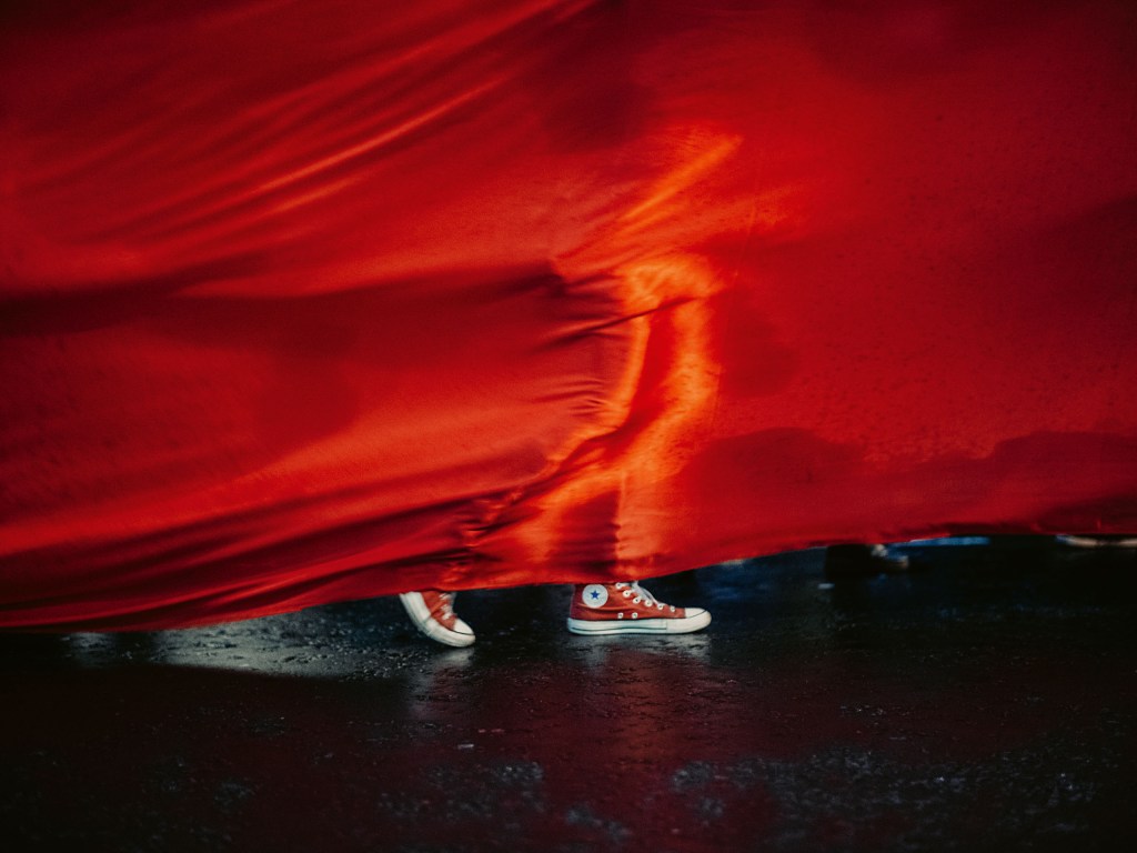a person wearing red sneakers behind a large piece of red material