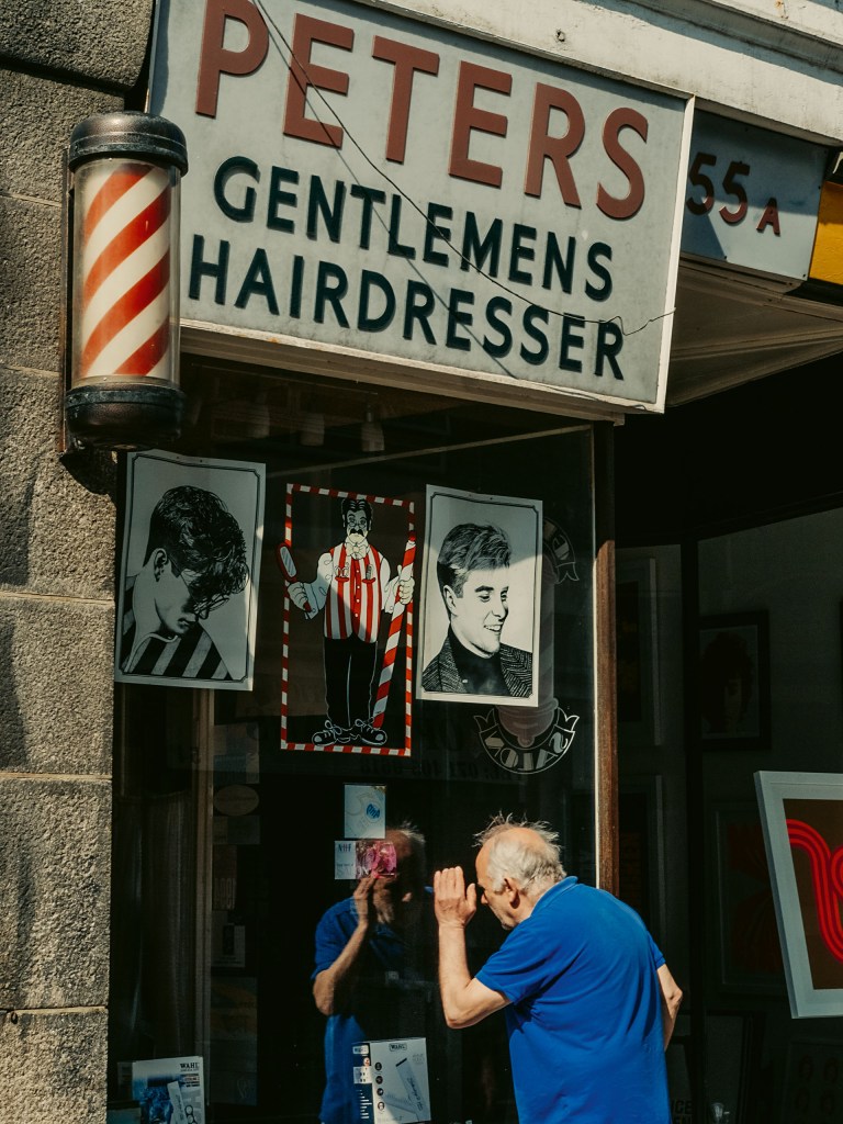 A colour image of a man standing outside a hairdresser
