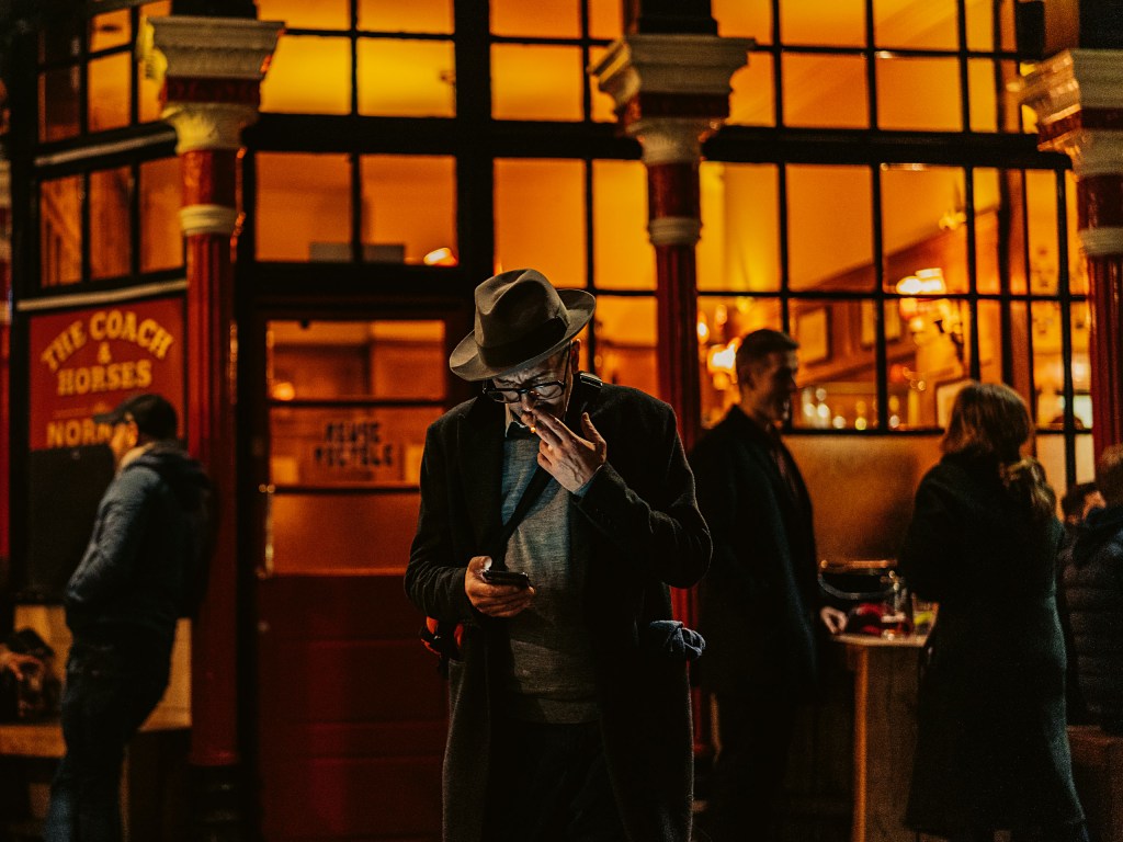 moody photo of man smoking and looking down at his phone