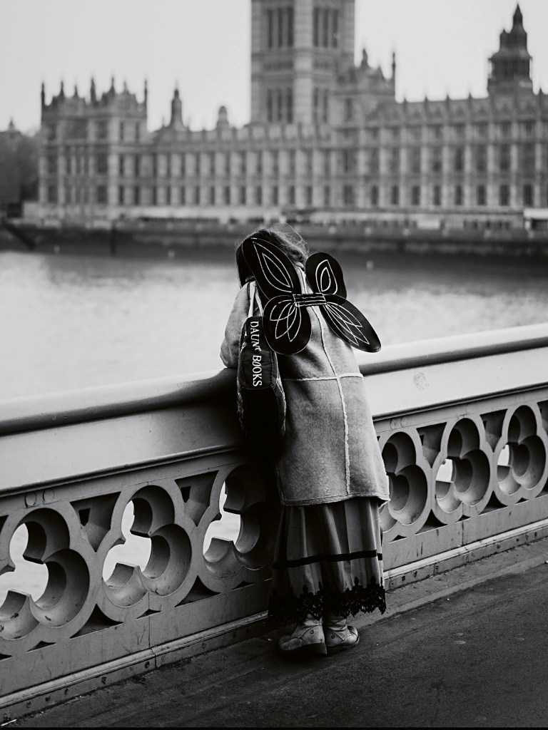 black and white photo of the back of a girl with butterfly wings peering over a bridge