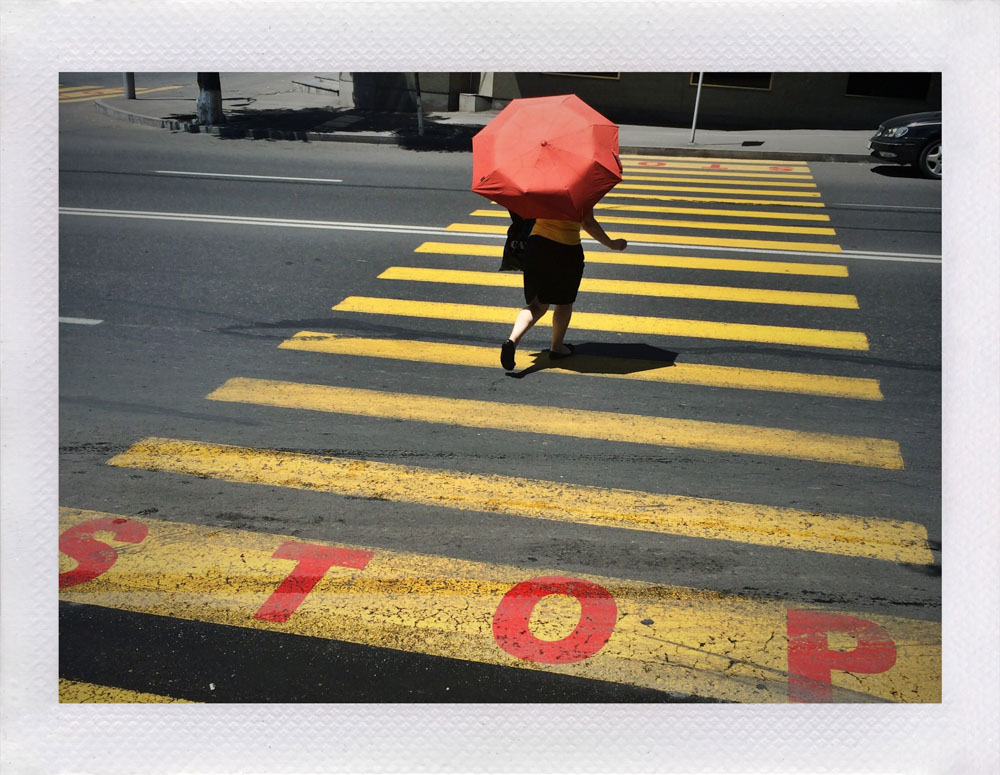 A person holding a red umbrella using a pedestrian crossing
