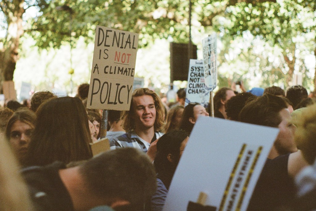 Photograph taken on Kodak Ultramax 400, showing a young man in a crowd holding a sign reading 'Denial is not climate policy'