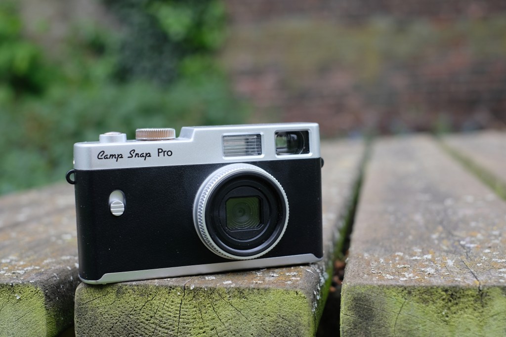 Photograph of the Camp Snap CS-PRO digital compact camera on a table facing forwards, lens visible