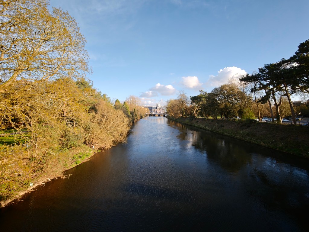 A landscape image showing blue sky, and a river, plus a sports stadium