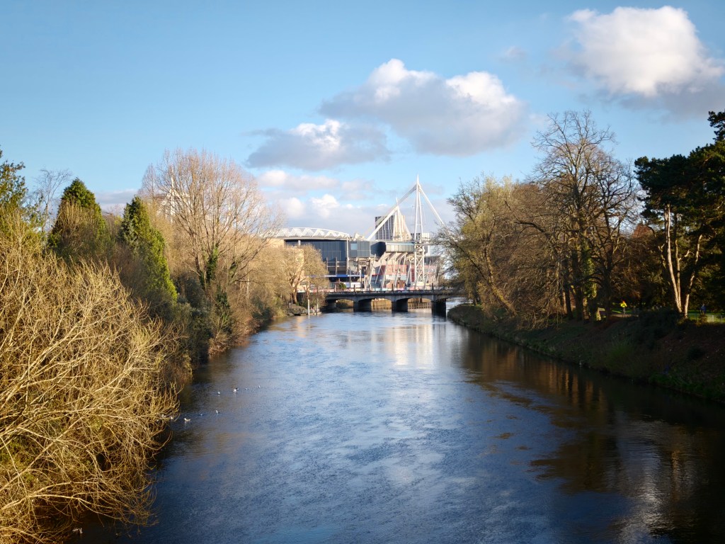 A landscape image showing blue sky, and a river, plus a sports stadium