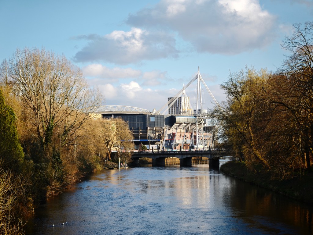 A landscape image showing blue sky, and a river, plus a sports stadium