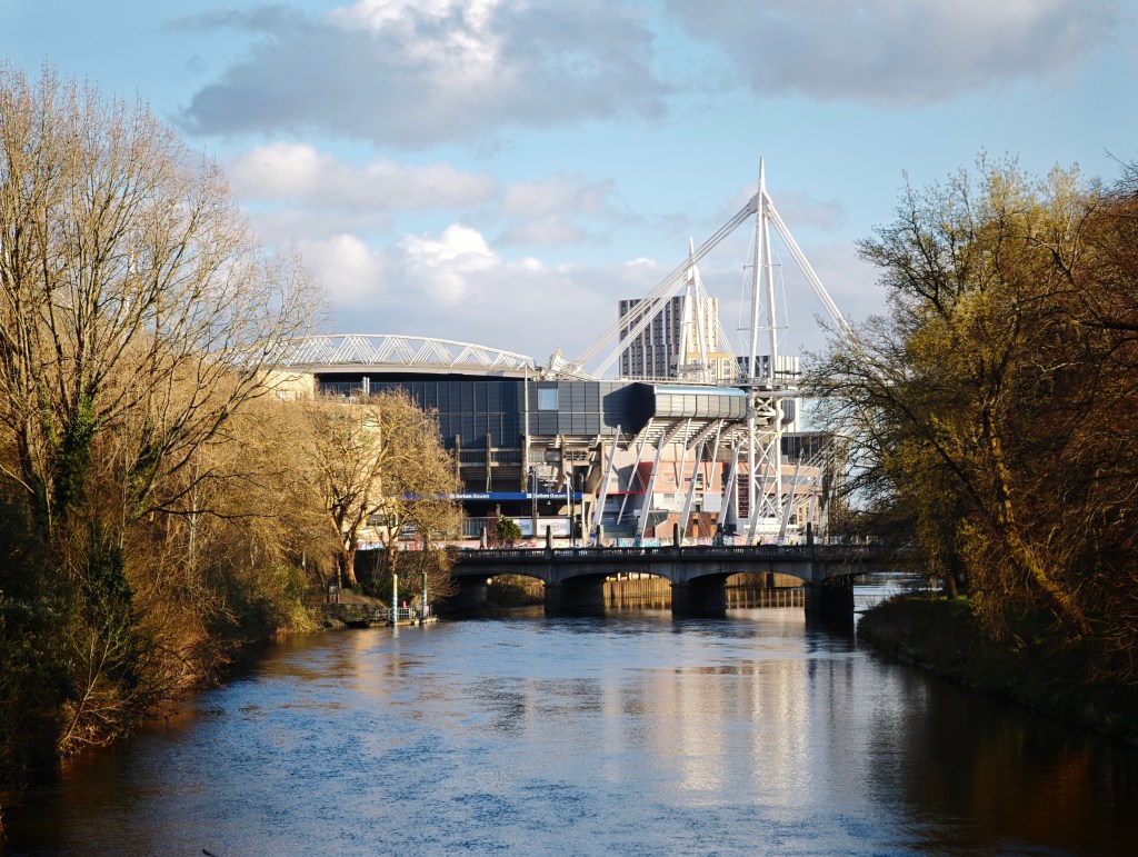 A landscape image showing blue sky, and a river, plus a sports stadium